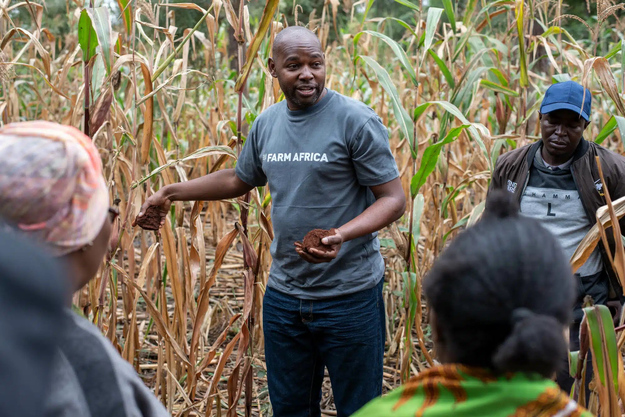 A man talking to another man and 2 women in the foreground. He is wearing a tshirt that says Farm Africa on it.