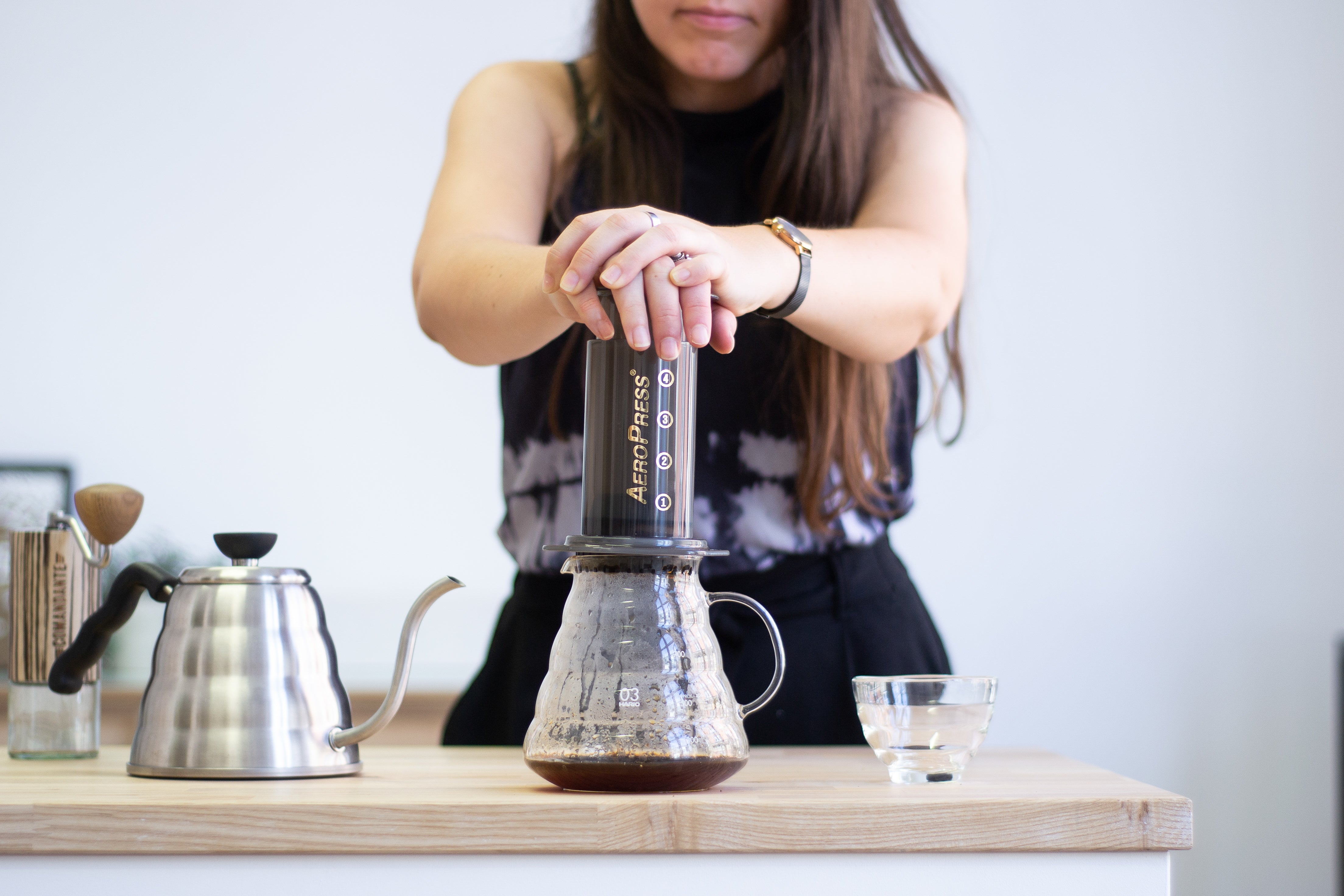 A woman using both hands to plunge an AeroPress full of decaf coffee on a wooden counter.