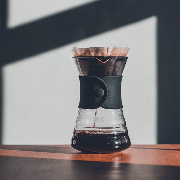 Hario V60 Drip Decanter Pour Over Coffee Maker with coffee dripping into it, on a wooden table