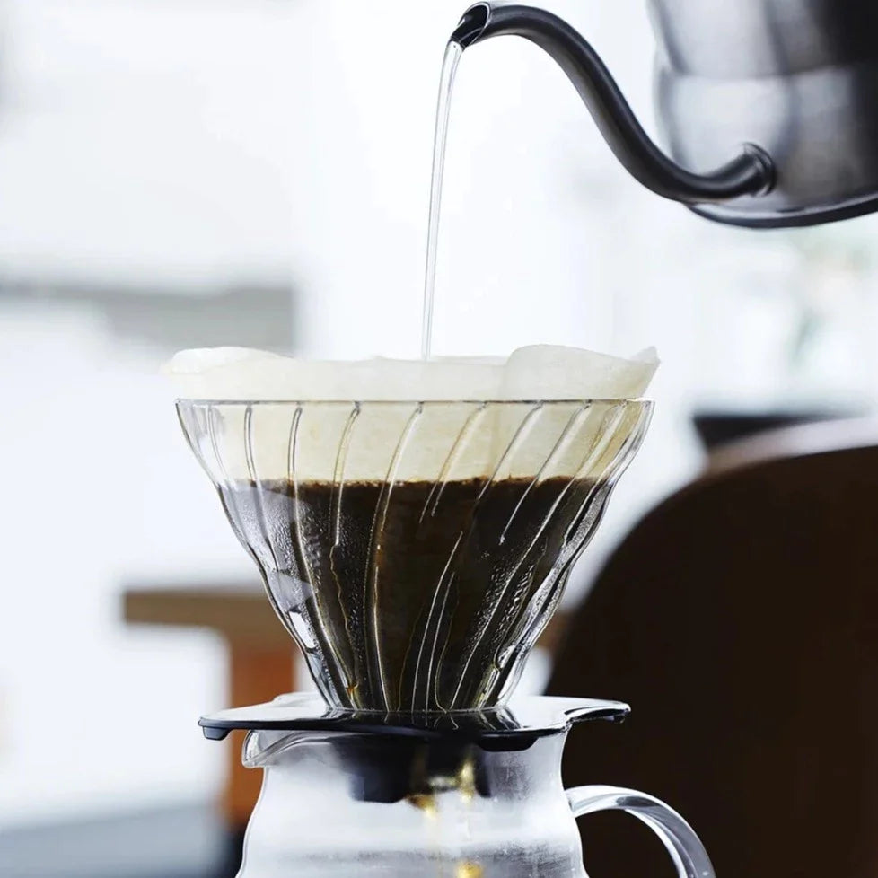 An image of a Hario V60 Glass Dripper with a filter paper and coffee in it, and water pouring in from a kettle.
