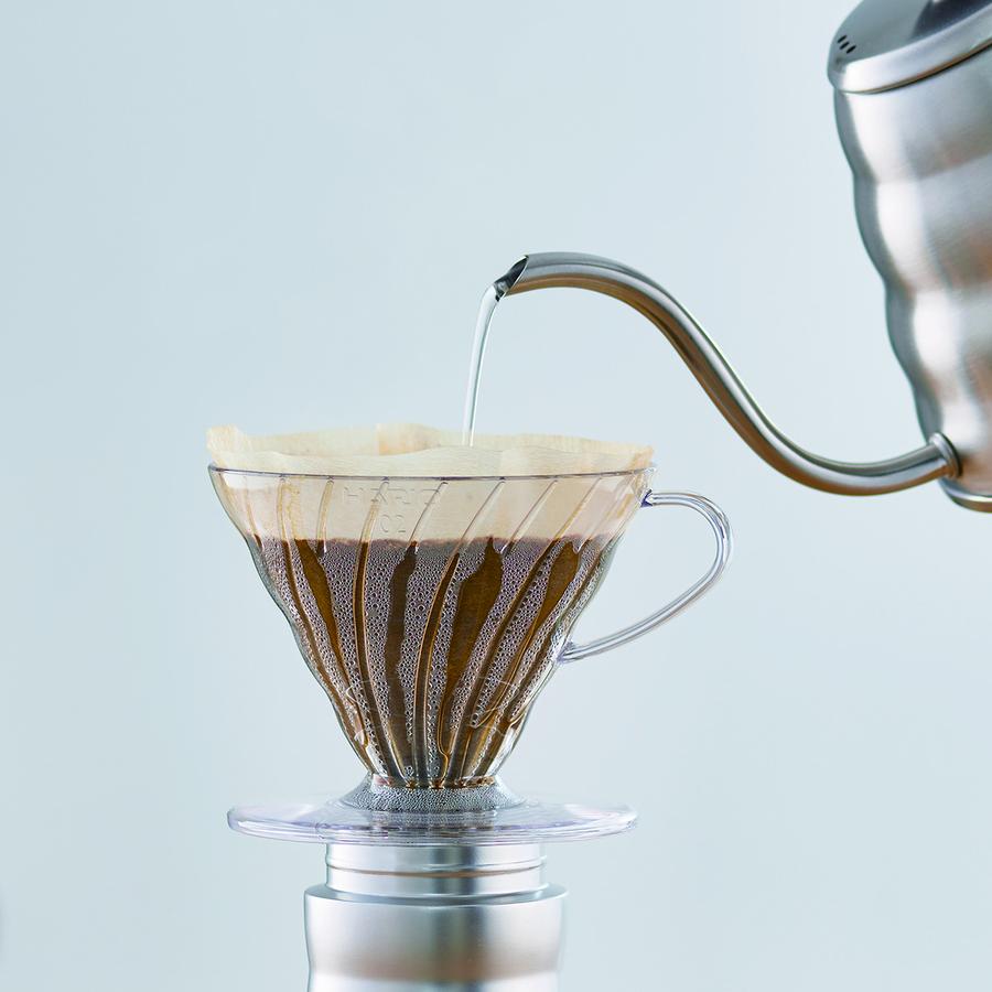 A plastic Hario 60 plastic dripper with a filter and coffee in it and water pouring in from a kettle.