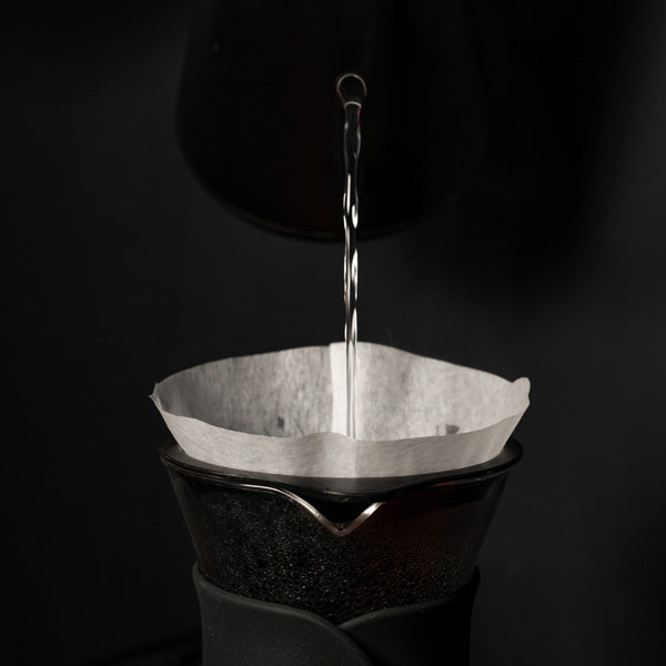 Water pouring from a kettle into a white filter sat inside a hario V60 decanter