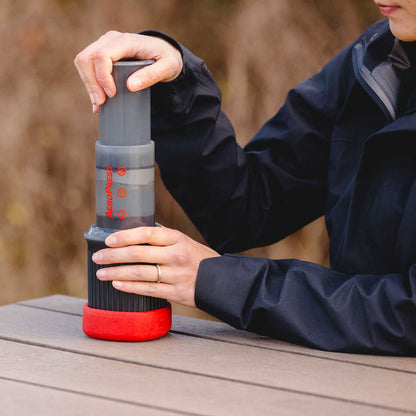 A person pressing down on the top of an aeropress go travel coffee maker
